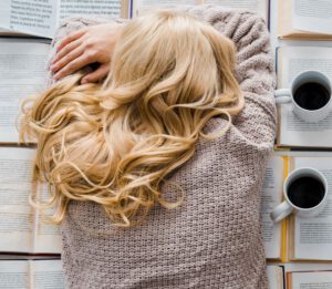 Erschöpfte Frau ist auf ihren Büchern eingeschlafen. Neben ihr stehen zwei volle Tassen Kaffee.