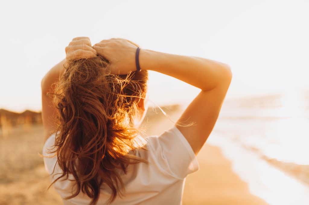 Rückenansicht einer Frau, die mit dem Gesicht zur Sonne steht und mit der Sonnenstrahlung Vitamin D aufbaut.