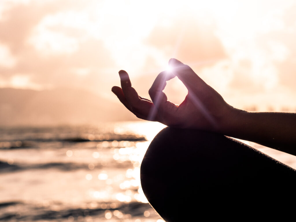 Ausschnitt von einer Frauenhand mit Mudra, Meditation gegen Stress im Sonnenuntergang am Meer.
