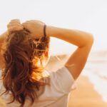 Rückenansicht einer Frau, die mit dem Gesicht zur Sonne steht und mit der Sonnenstrahlung Vitamin D aufbaut.