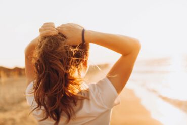 Rückenansicht einer Frau, die mit dem Gesicht zur Sonne steht und mit der Sonnenstrahlung Vitamin D aufbaut.